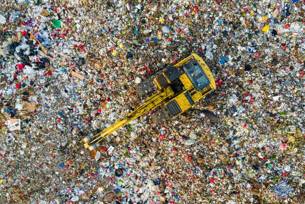 Aerial shot of a landfill with a yellow excavator in South Tangerang, Indonesia.